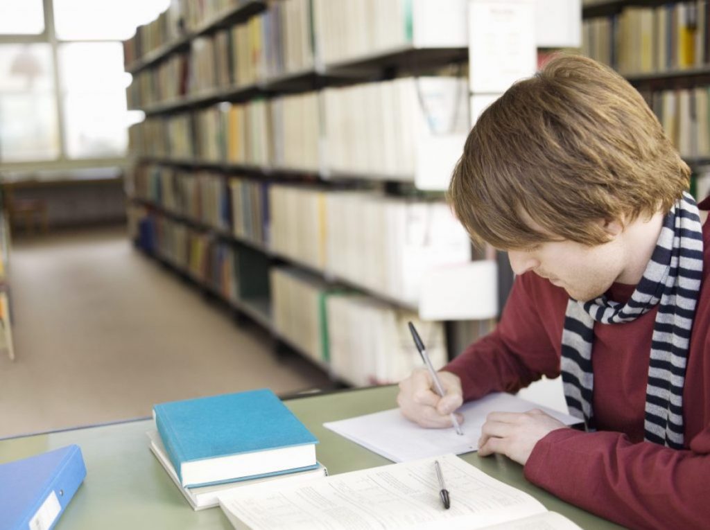 Image of male student in a library working on various Descriptive Essay Topics